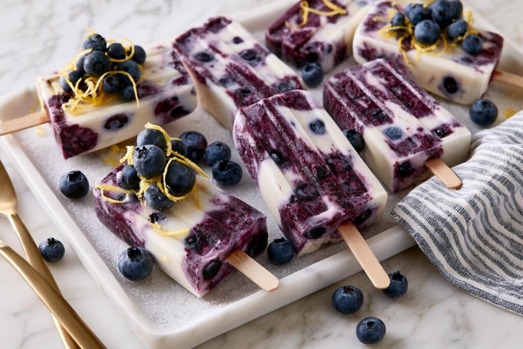Blueberry protein popsicles on a chilled tray with wild blueberries and lemon zest garnish