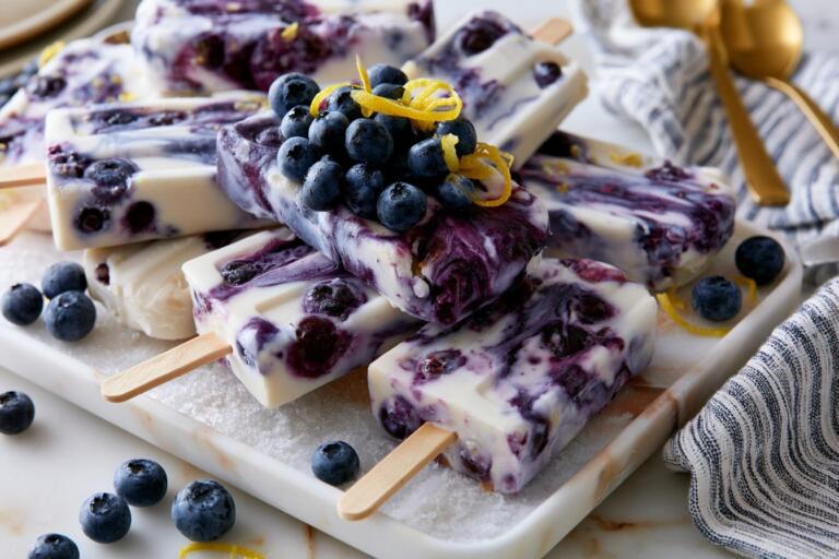 Blueberry protein popsicles on a chilled tray with wild blueberries and lemon zest garnish