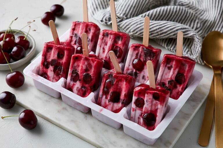 Cherry protein popsicles on a chilled tray with dark chocolate flecks and fresh cherries