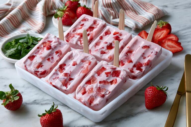 Plated strawberry protein popsicles on a chilled tray with fresh strawberry chunks and mint